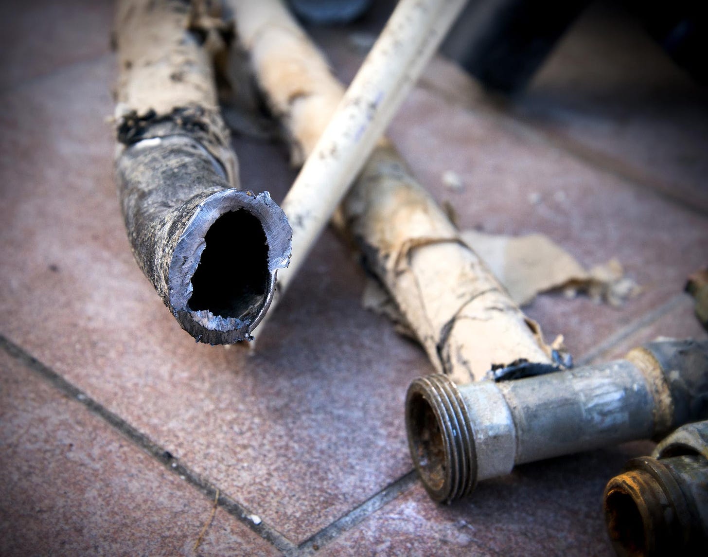 Lead pipes, broken open to show their toxic interiors, lay on a tiled surface.