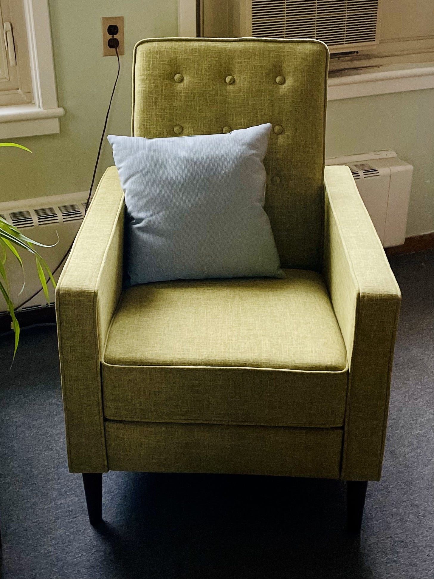 A green chair with a light blue pillow on in with tufted buttons.