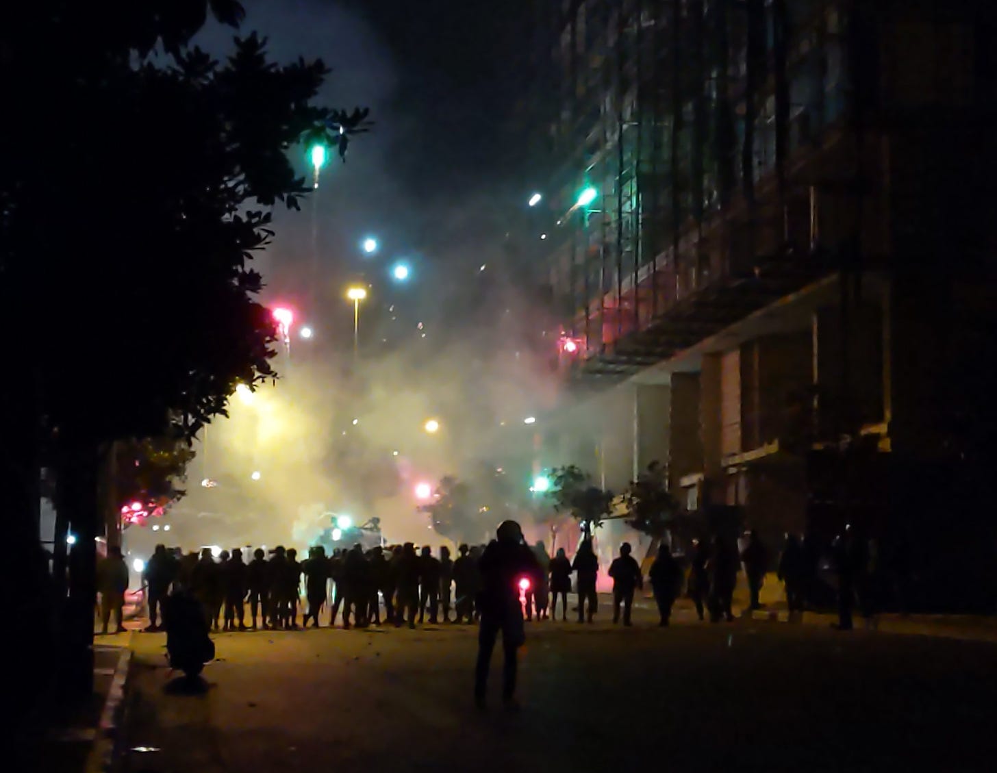 Colorful flares blast up into a night sky above a crowd of armed guards