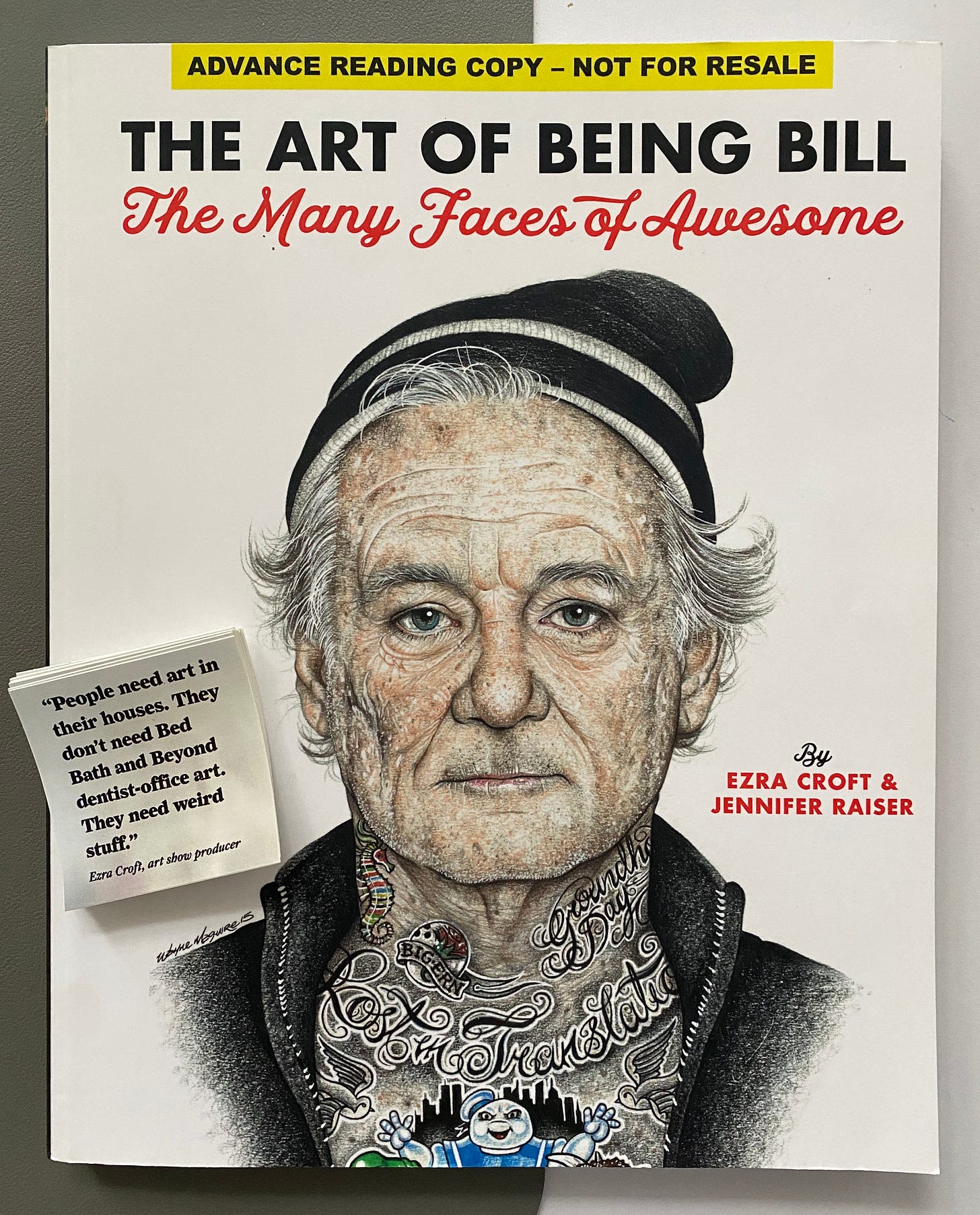 A copy of the pre-sale book "The Art of Being Bill" by Ezra Croft and Jennifer Raiser with some stickers sitting on top. The stickers read "People need art in their houses. They don't need Bed Bath and Beyond dentist-office art. They need weird stuff."