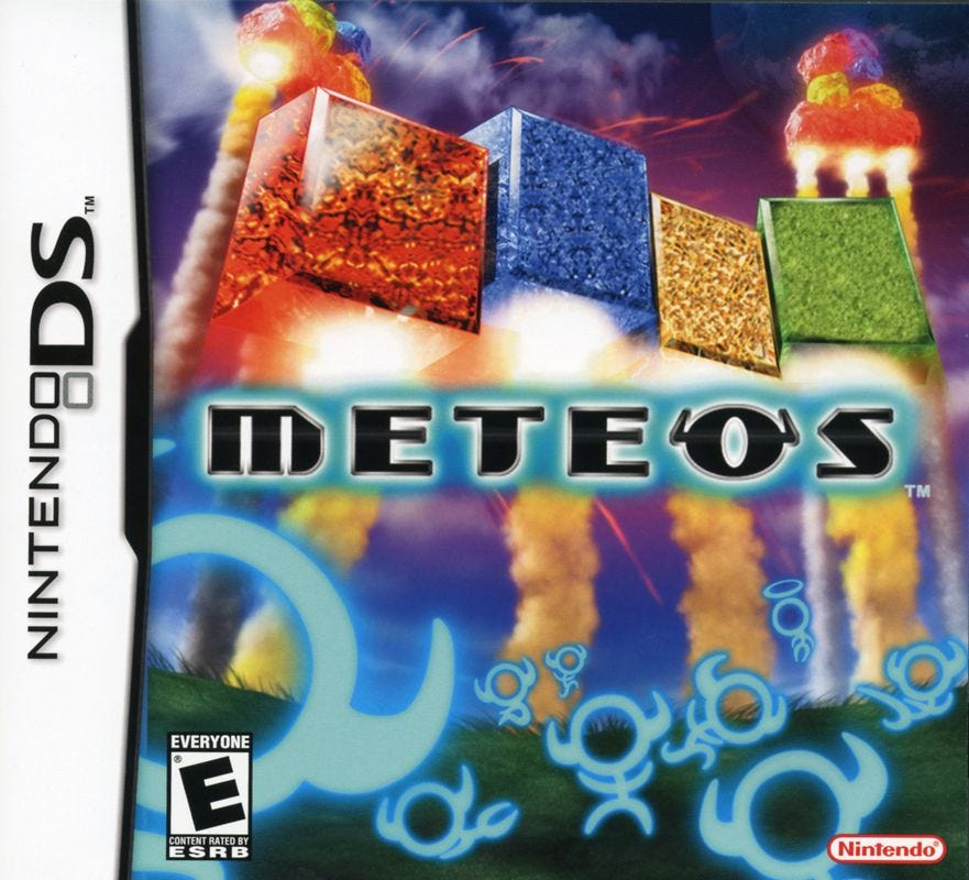 A scan of the Nintendo DS box art for Meteos, which shows a very zoomed in view of how the game works, in the sense that blocks are fallig from the sky while others are being rocketed back into it, while little alien creatures fly all over the place.