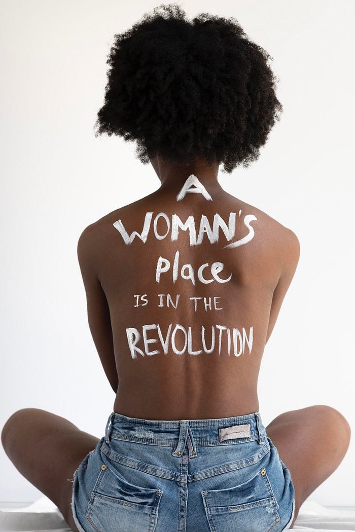 close up on a woman’s back with the words “a woman’s place is in the revolution”