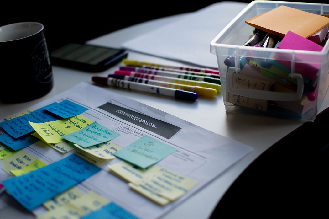 sticky notes on a piece of paper titled “Experience Brief” surrounded by design tools — pens, phone, paper, coffee cup