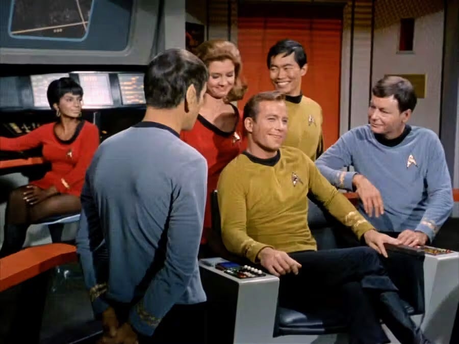 Captain Kirk sitting in his command chair on the bridge of the starship Enterprise, surrounded by crew members (source: CBS Studios startrek.com).