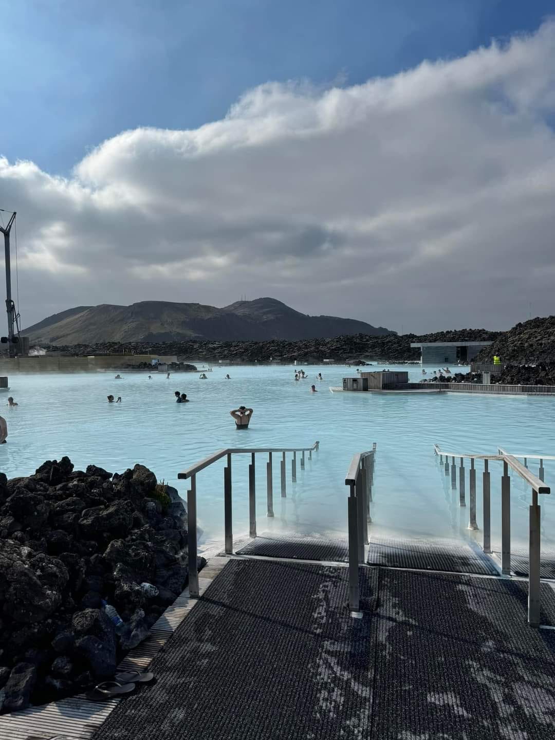 a group of people in a blue lagoon with heat rising and a steaming mountain in the background