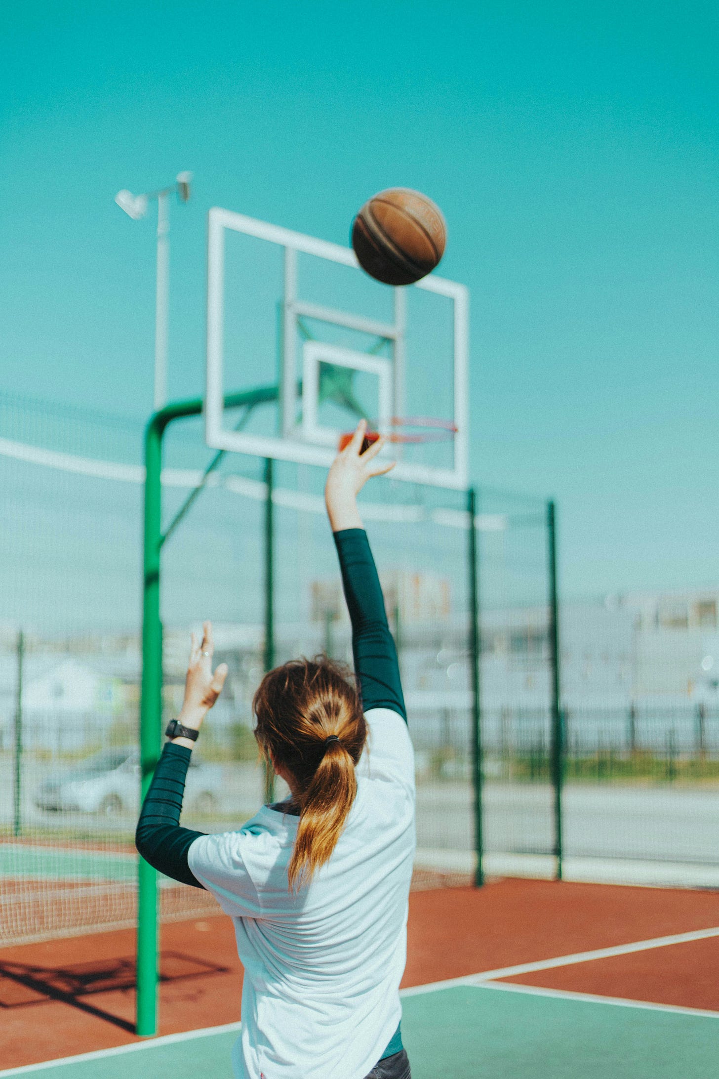 Woman with poney tail throwing a basketball at a hoop. Will she sink the shot?