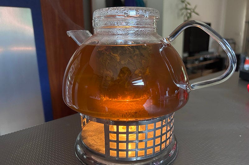 Glass teapot sits on a warmer stand with a candle lit underneath it.