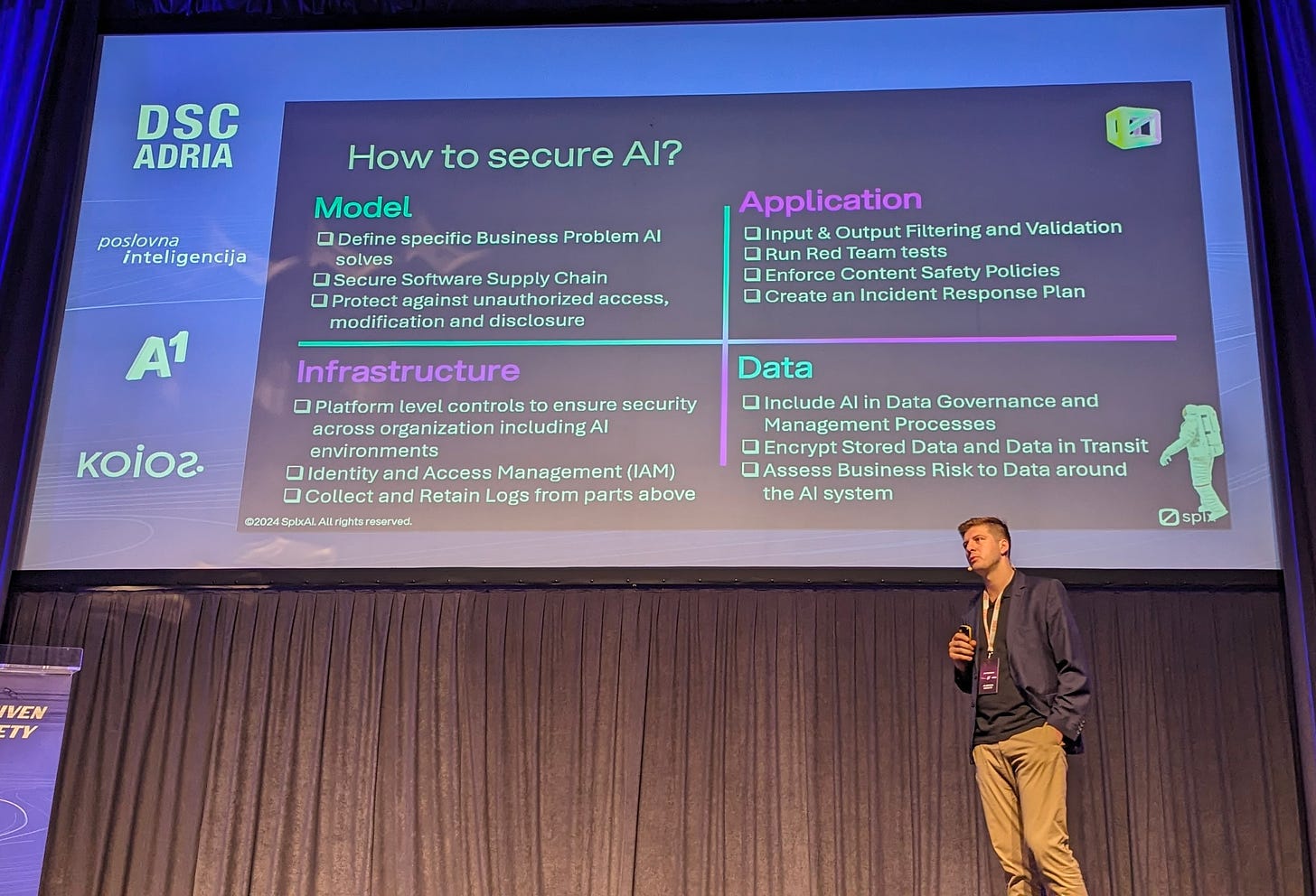 A conference speaker presenting a slide titled "How to secure AI?". The slide is split into four sections and corresponding points: Model: Define specific business problem AI solves; Structure software supply chain; protect against unauthorized access, modification and disclosure. Infrastructure: Platform level controls to ensure security across organisations; Identity and access management; Collect and retain logs. Data: Include AI in Data Governance and management processes; Encrypt stored data and data in transit; Address business risk to data around the AI system. Application: Input and output filtering and validation; Run red team tests; Enforce content safety policies; Create an incident response plan