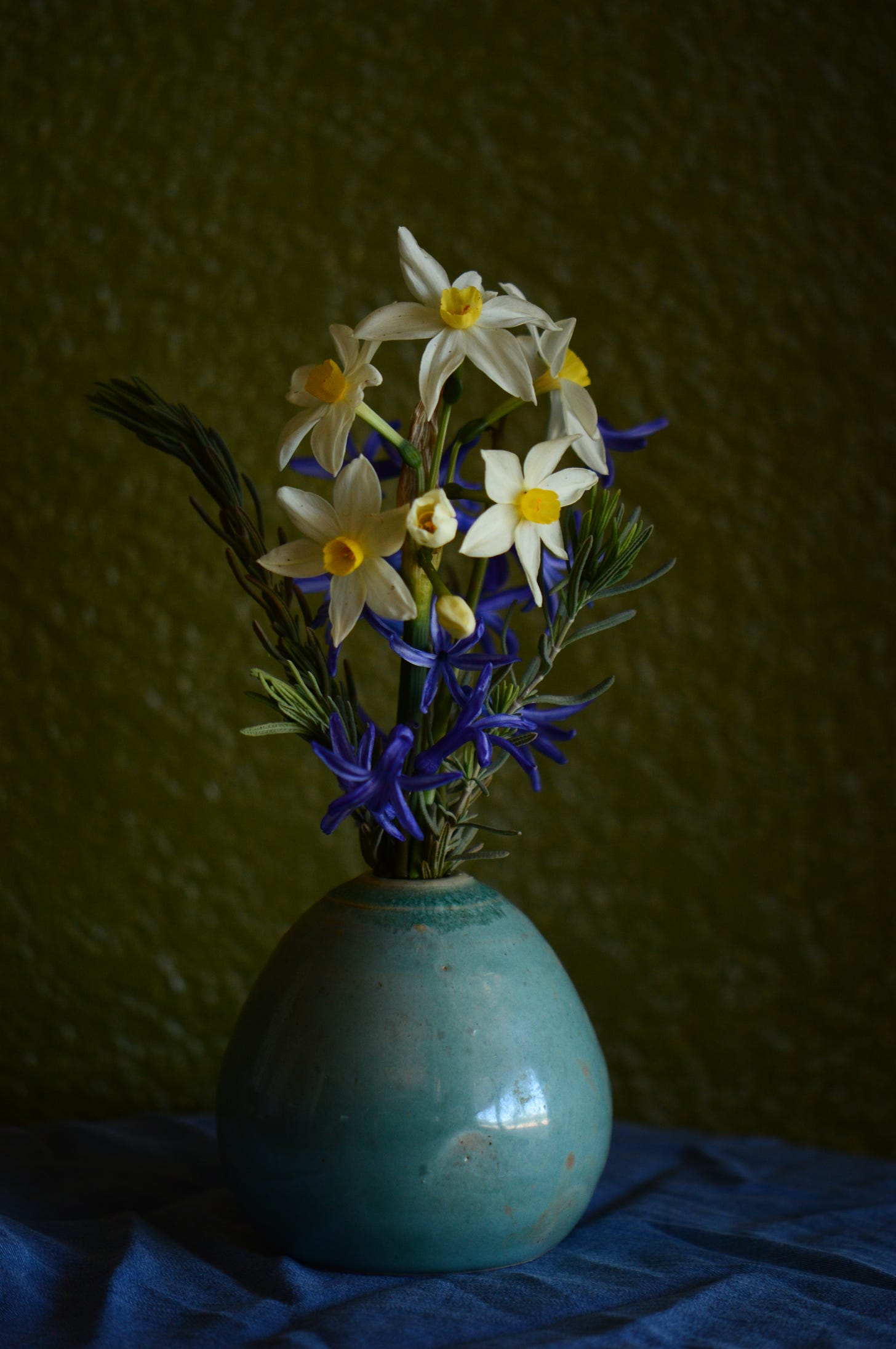 A spray of white and yellow narcissus with blue Roman hyacinths in a pale aqua-colored art vase