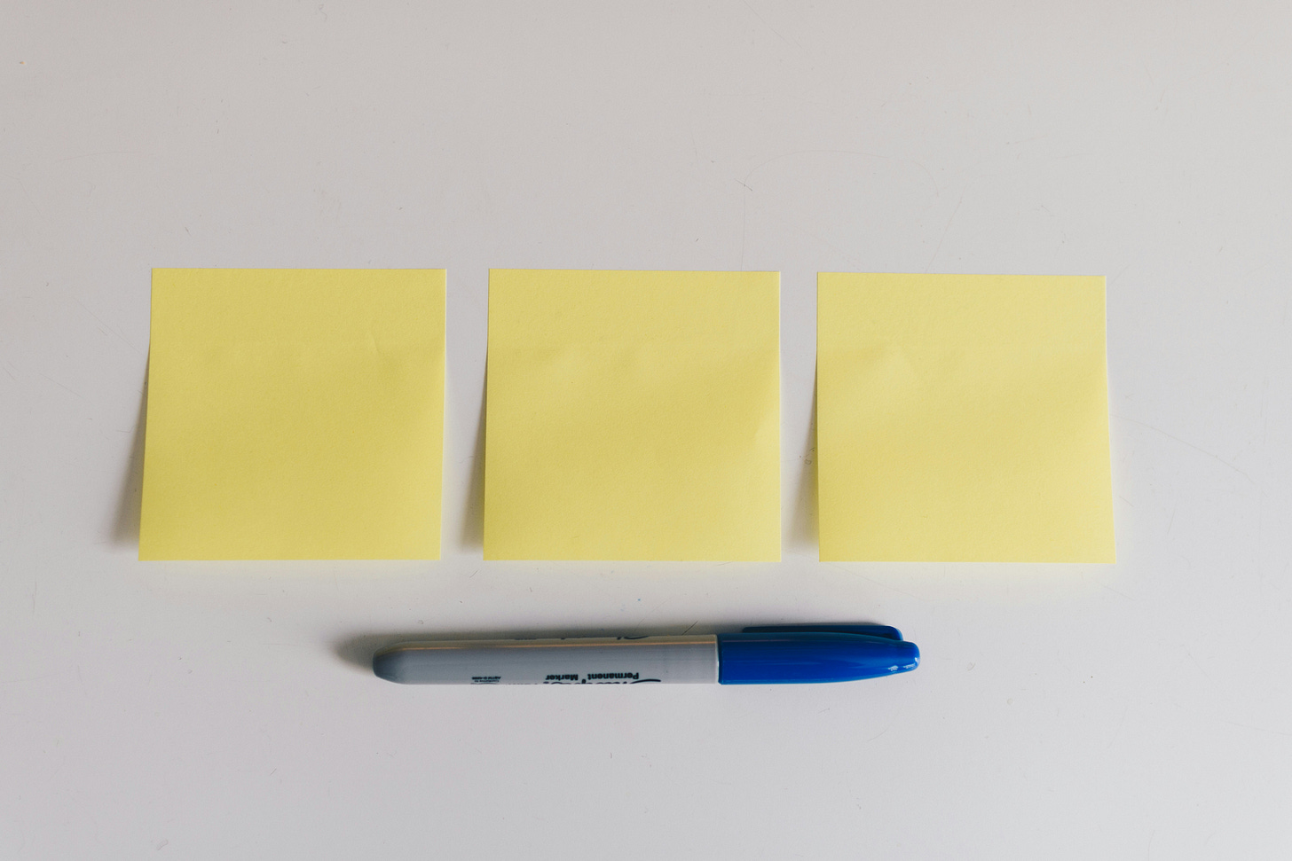 A set of three yellow sticky notes on a white backround with a sharpie lined up underneath