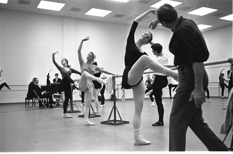 George Balanchine teaching company class, dancers at the barre in attitude front looking under their raised arm