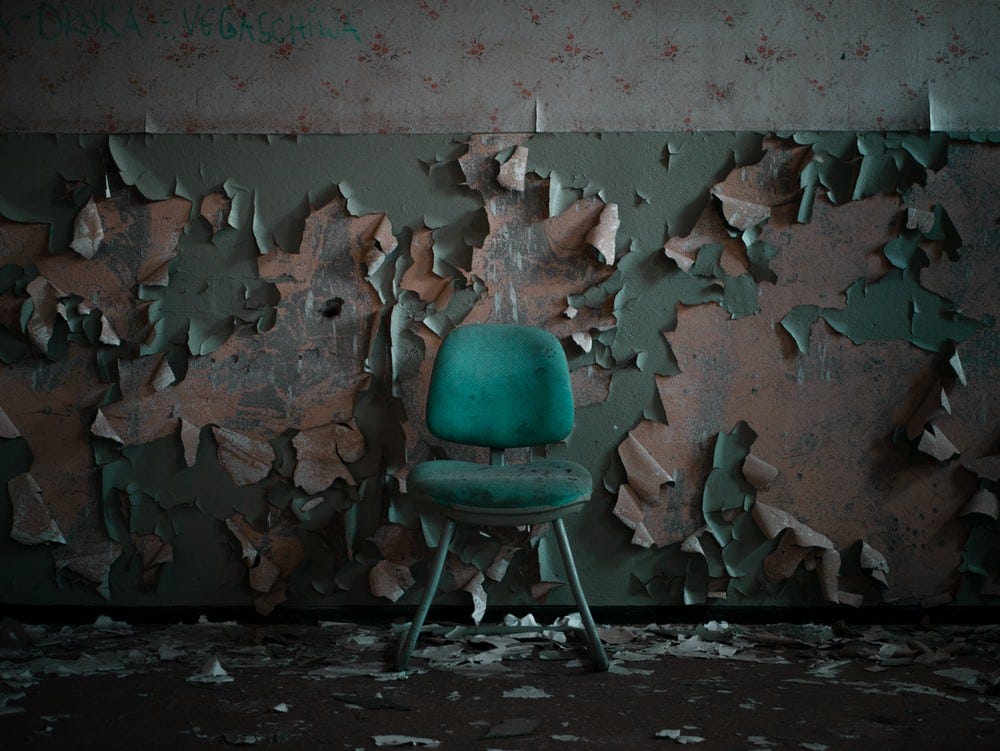A dirty blue plastic chair in front of a wall with dirty peeling paint.