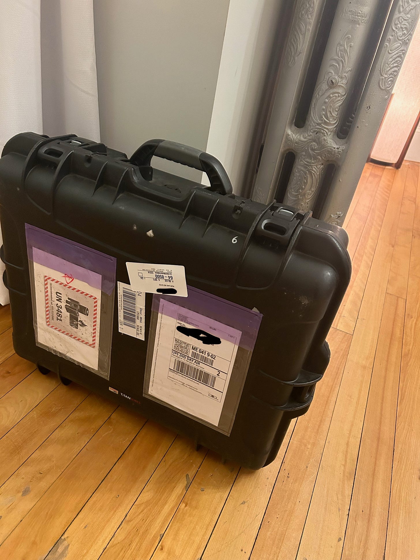 a black plastic suitcase covered in labels, on a hardwood floor