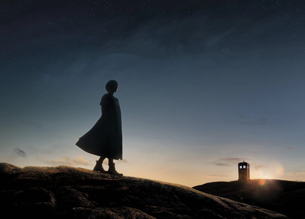 This image shows the Thirteenth Doctor (played by Jodie Whittaker) standing on a ridgeline gazing at her TARDIS, which sits in the distance atop another ridgeline. Thirteen's back is to camera and she stands mostly in shadow, with the sun just rising above and behind the distant TARDIS. This image shows the Thirteenth Doctor (played by Jodie Whittaker) standing on a ridgeline gazing at her TARDIS, which sits in the distance atop another ridgeline. Thirteen's back is to camera and she stands mostly in shadow, with the sun just rising above and behind the distant TARDIS.