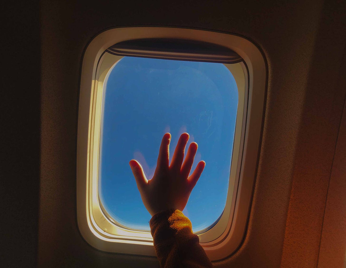 A child's hand splayed on an airplane window whose fingers are lit up by the sun. Photo credit: Nancy Forde. All rights reserved. nancyforde.com