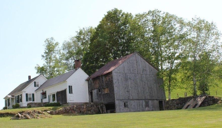 Vermont farmhouse with white clapboard siding, stone walls, and old barn