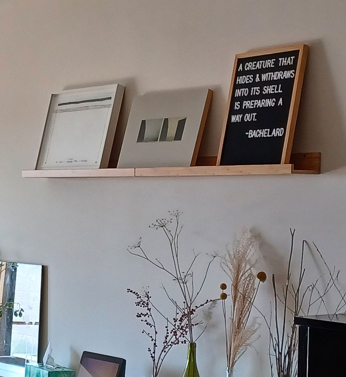 wooden shelf with framed artwork and bachelard quote above dried plants in vases