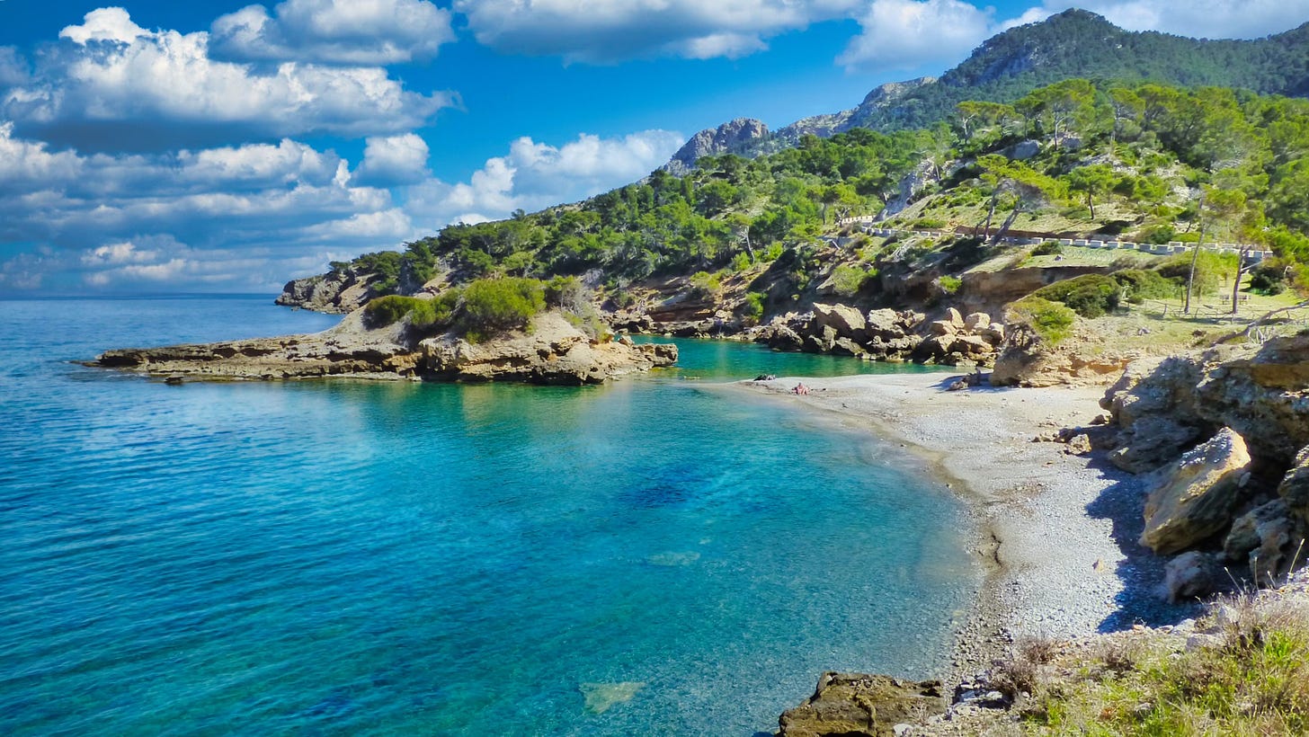 A tranquil view of the Bay of Alcudia in Mallorca, Spain, with crystal-clear turquoise waters and rugged cliffs, symbolizing the peaceful process of self-realization and reconnecting with hidden inner resources.