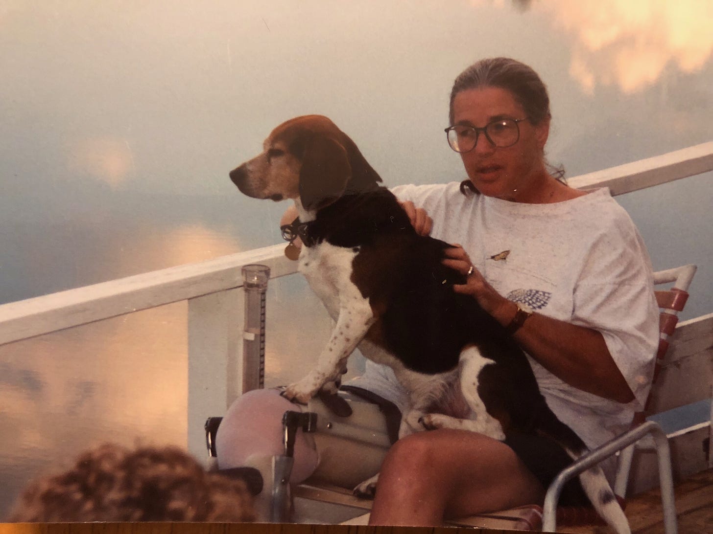 A woman with a beagle on her lap sitting on a deck
