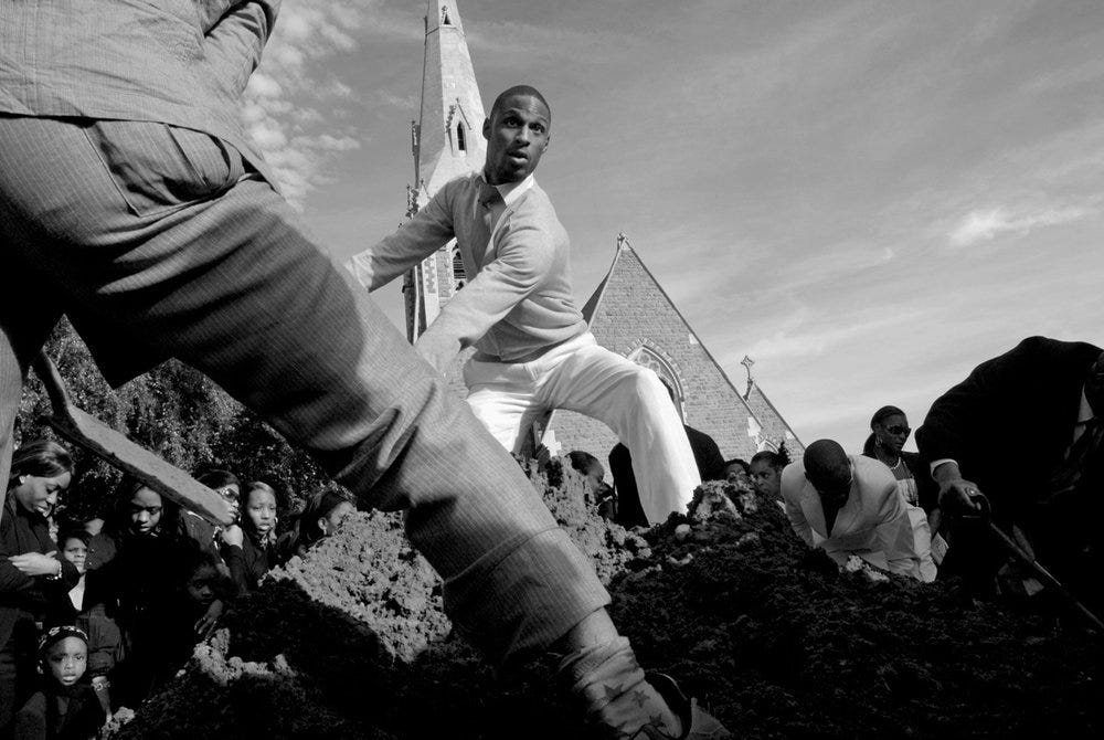 Men fill the grave of a young man who was shot, 2008. © Vanley Burke