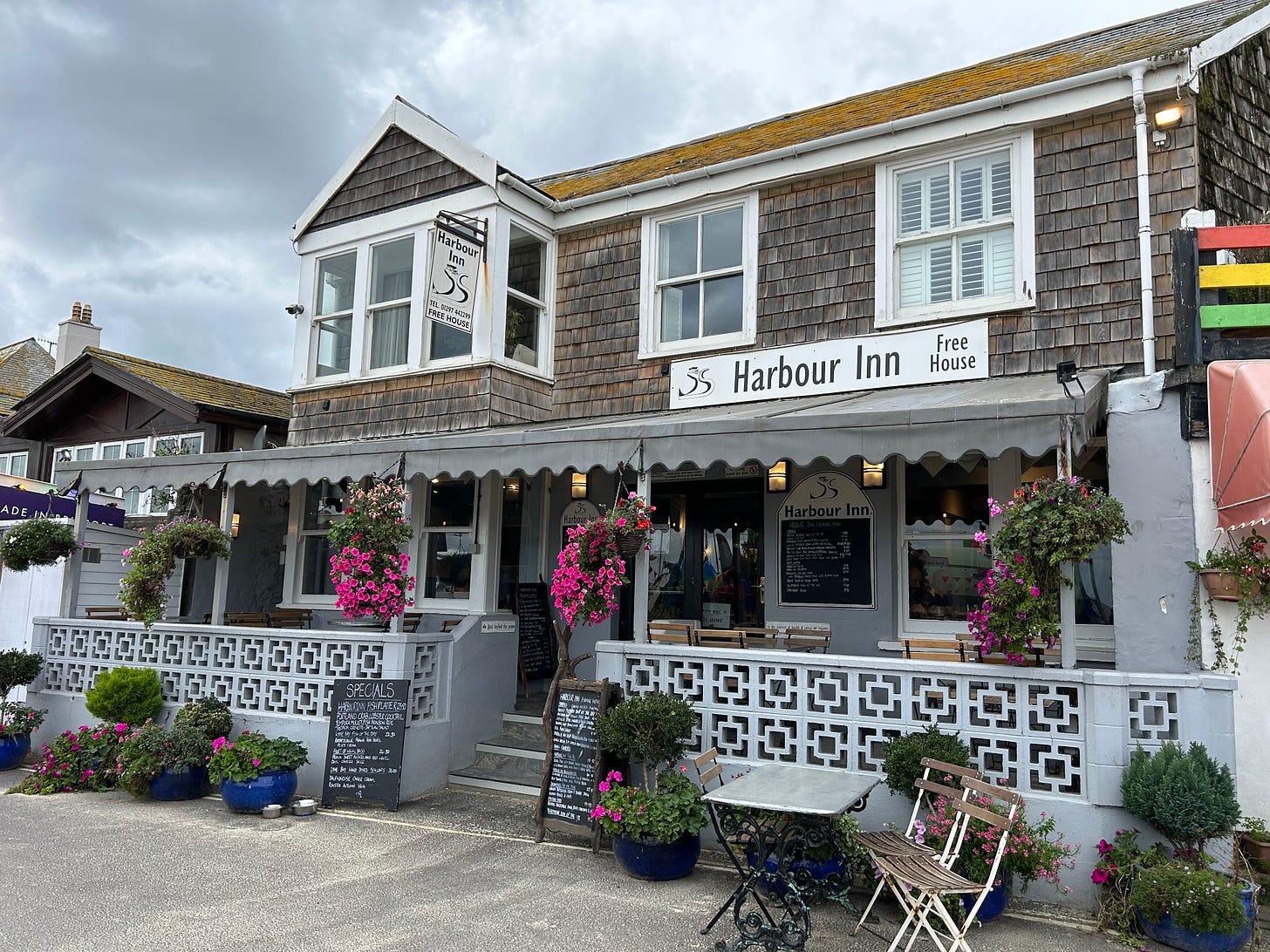 Harbour Inn, Marine Parade, Lyme Regis. There is an outside veranda for those days to sit out and enjoy food or a drink. The veranda is adorned with hanging baskets and pots of flowers are in front of the inn along with two menu boards. Image: Rolands' Travels