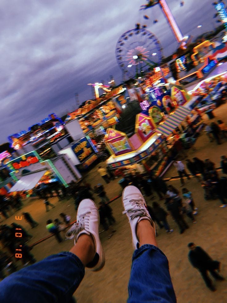 This may contain: the feet of a person standing in front of an amusement park with ferris wheel and carnival rides