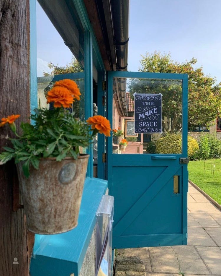 A blue open door and a pot of marigolds outside The Make Space