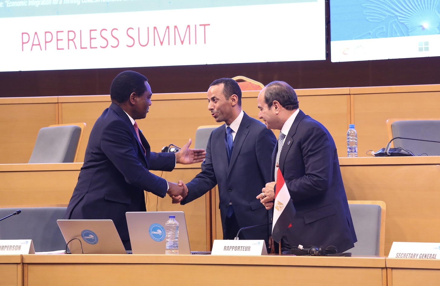 May be an image of 3 people, dais and text that says "PAPERLESS SUMMIT RPERSON COMESA RAPPORTEUR SECRETARYGENERAL GENERAL"