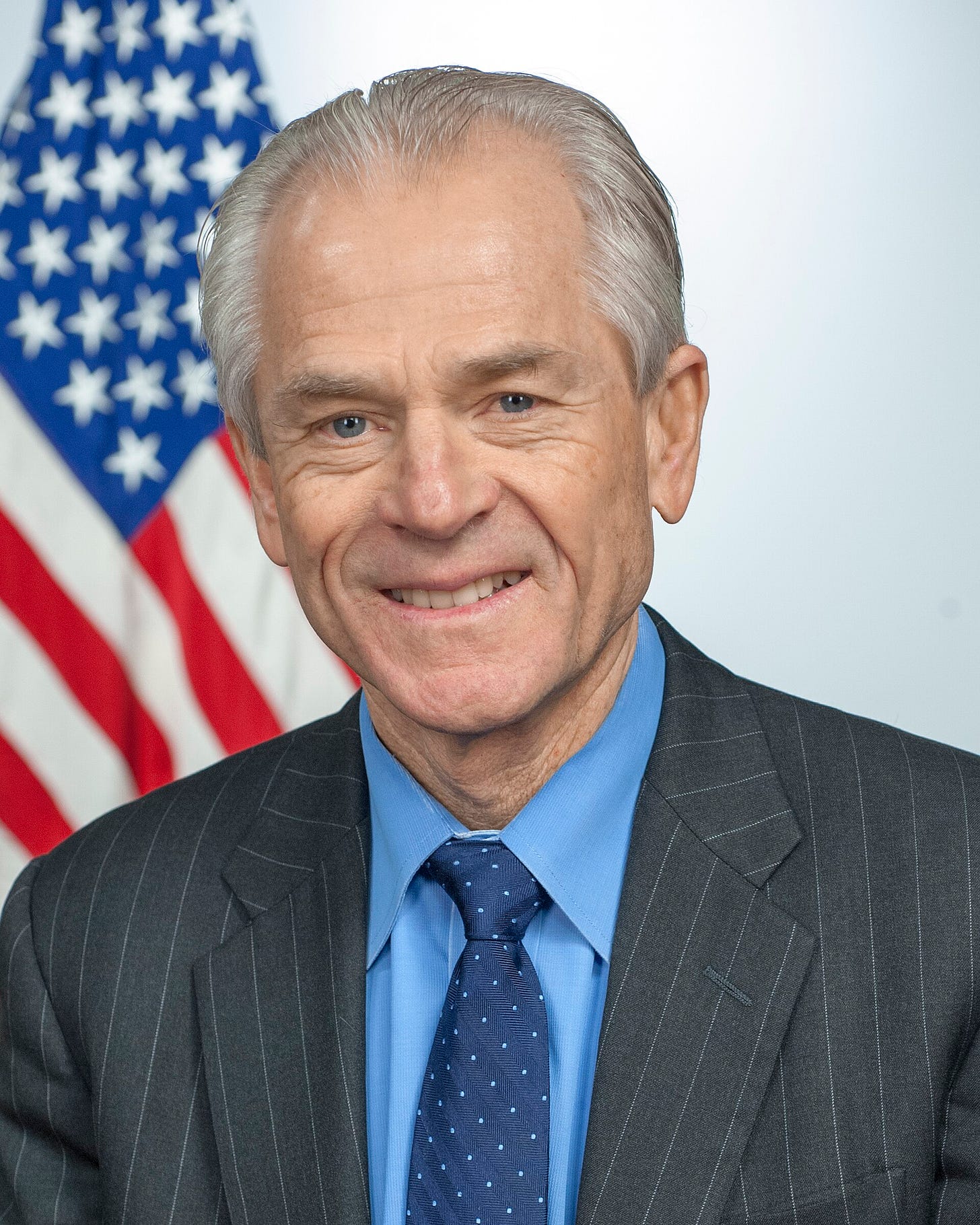 Navarro smiling, seated in front of an American flag