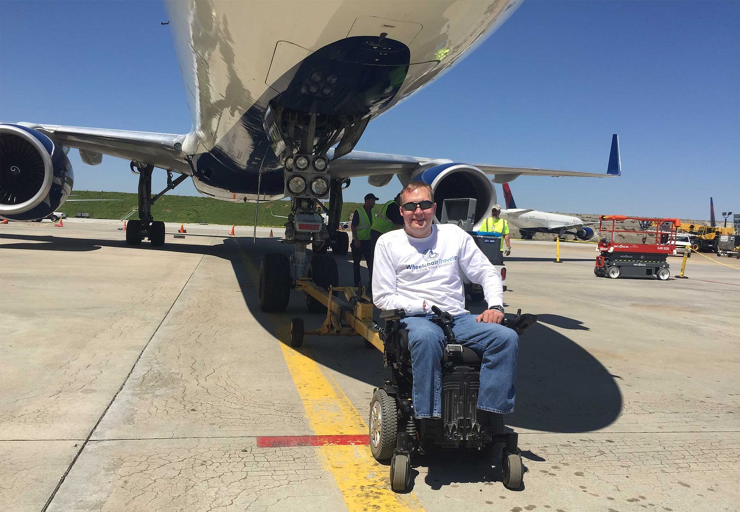 John seated in his wheelchair at the front wheel of a Delta Boeing 757 aircraft.