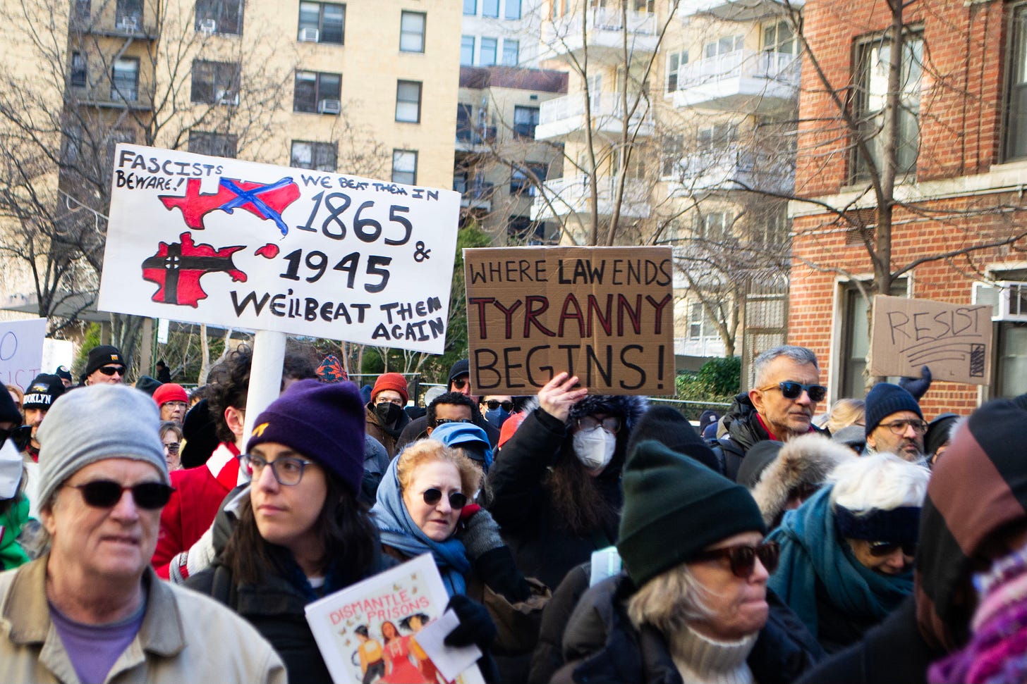 Protesters hold up signs, with one saying "Fascists beware! We beat them in 1865 and 1945 and we'll beat them again," another saying "Where law ends, tyranny begins," and a third simply saying "Resist." Protesters hold up signs, with one saying "Fascists beware! We beat them in 1865 and 1945 and we'll beat them again," another saying "Where law ends, tyranny begins," and a third simply saying "Resist."