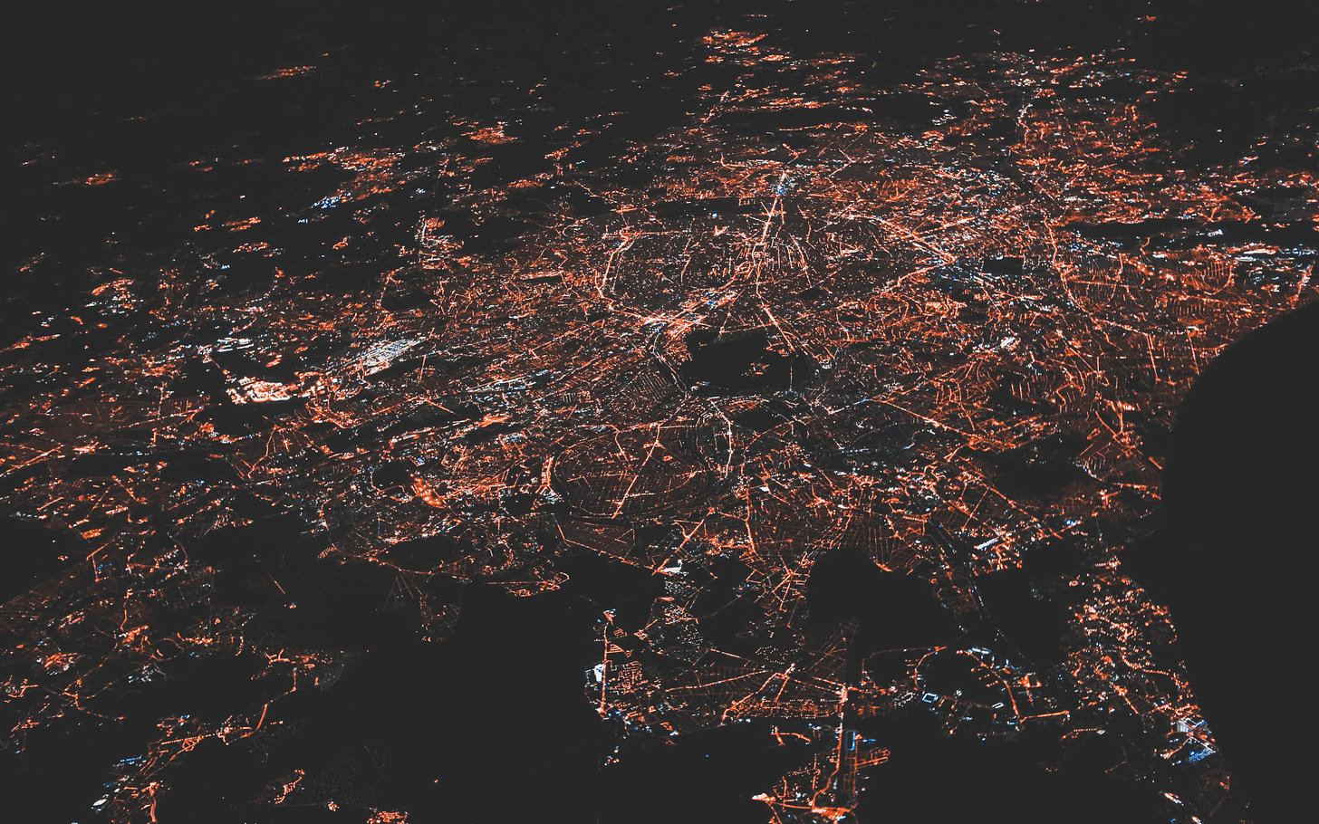 An aerial view of a city at nighttime. Orange lights punctuate a black background.