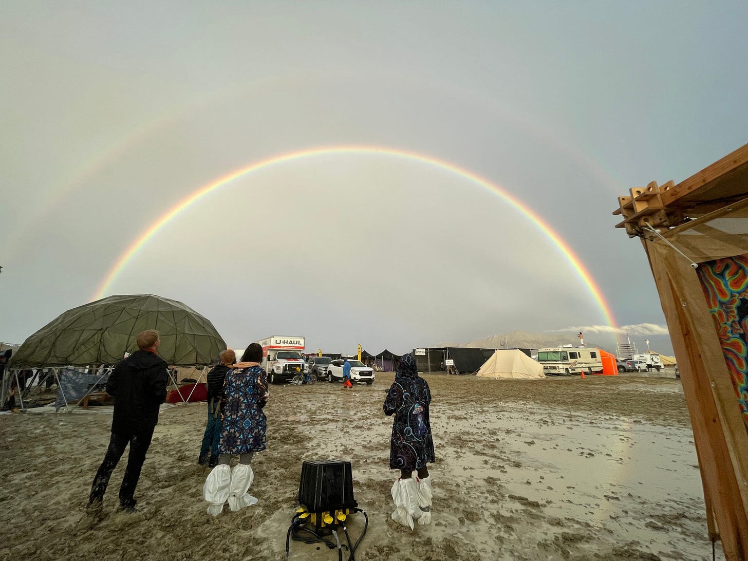 Attendees look at a double rainbow over flooding on a desert plain on September 1, 2023, after heavy rains turned the annual Burning Man festival site in Nevada's Black Rock desert into a mud pit. Tens of thousands of festivalgoers were stranded September 3, in deep mud in the Nevada desert after rain turned the annual Burning Man gathering into a quagmire, with police investigating one death. Video footage showed costume-wearing "burners" struggling across the wet gray-brown site, some using trash bags as makeshift boots, while many vehicles were stuck in the sludge.