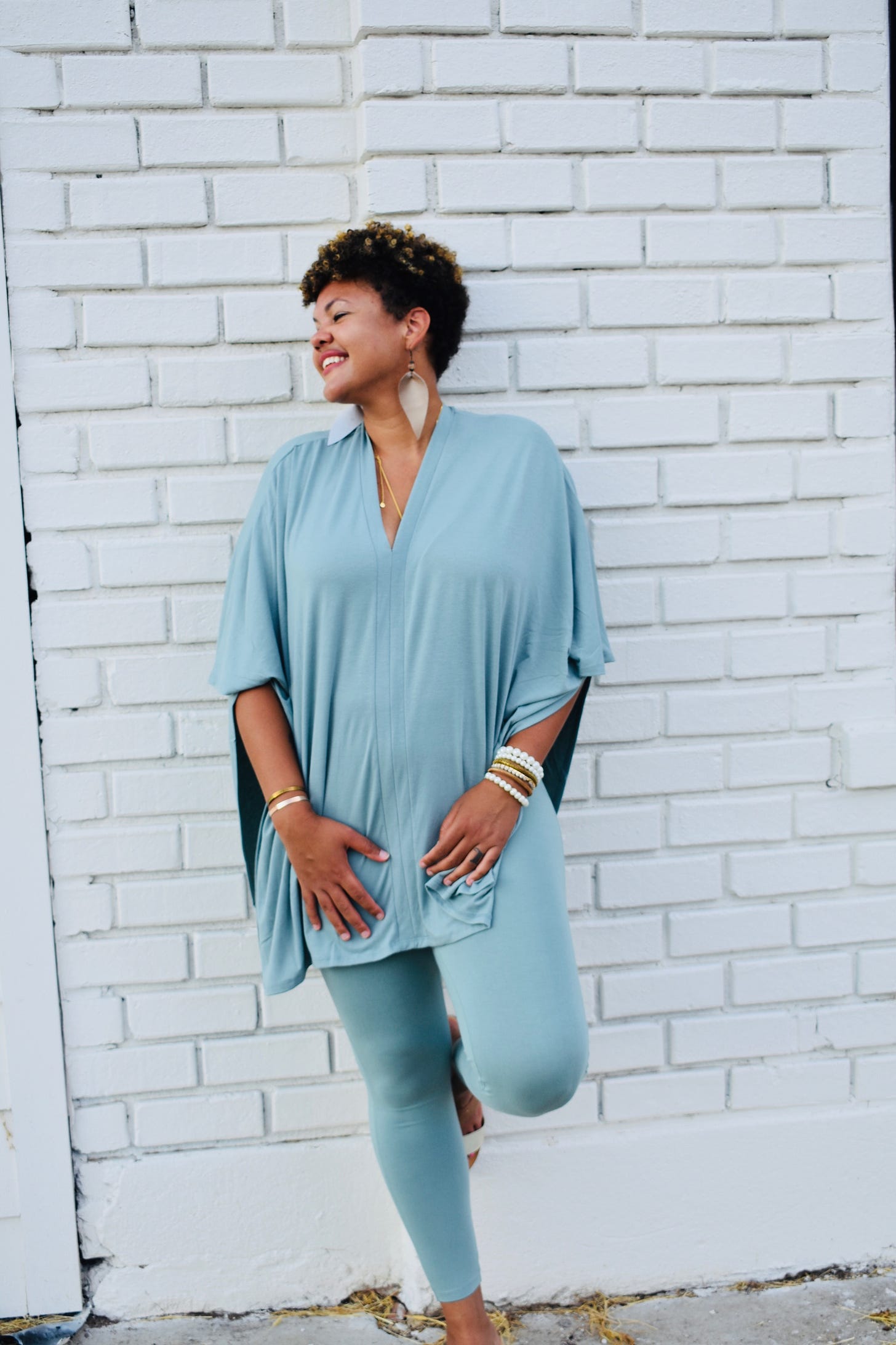 Headshot of today's guest, Whitney Trotter, standing against a white brick wall wearing a blue outfit and smiling