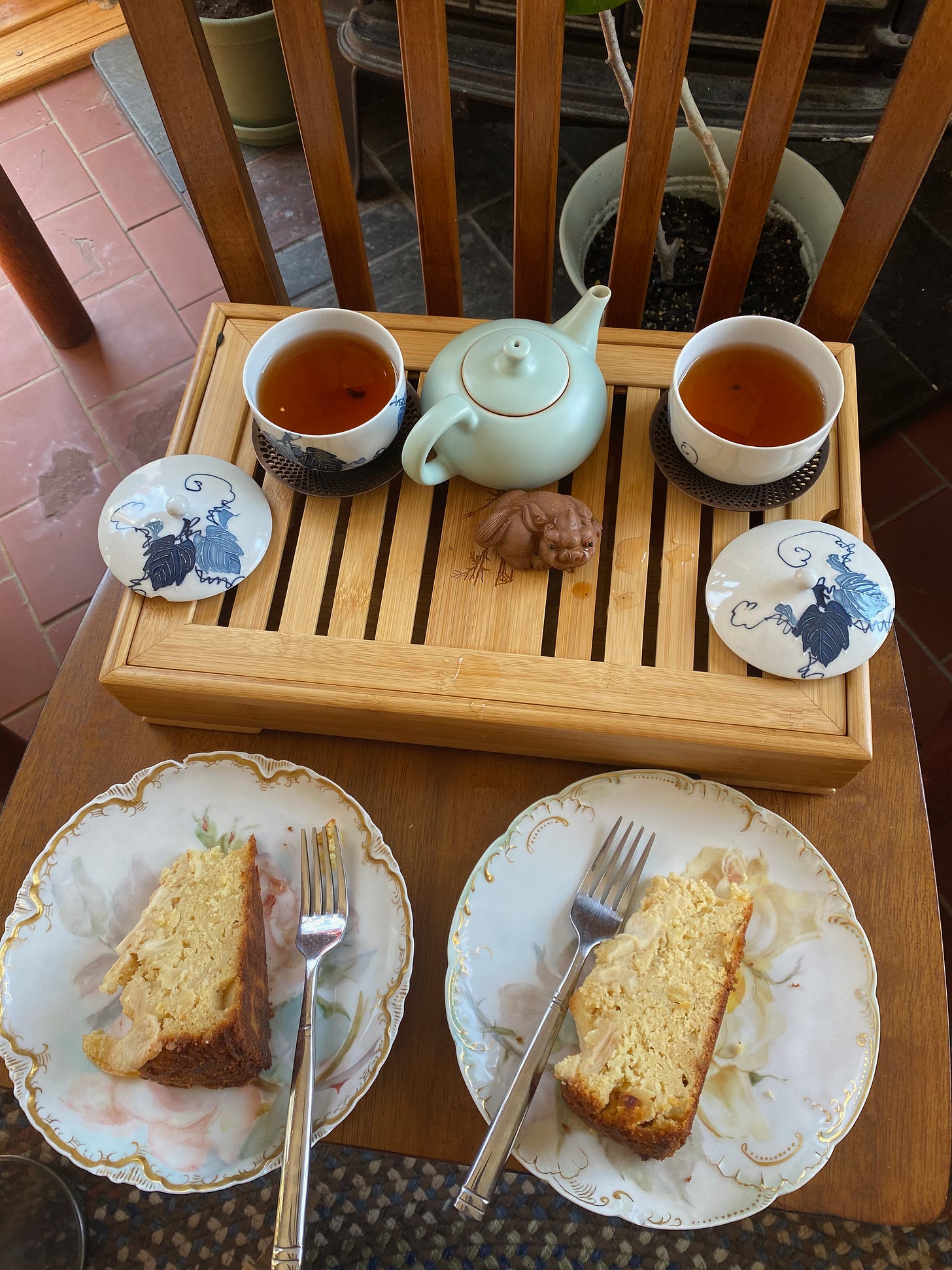 A tea tray on a chair: two small cups of tea, a dragon tea friend, a small porcelain teapot, and two plates of apple-almond cake. 