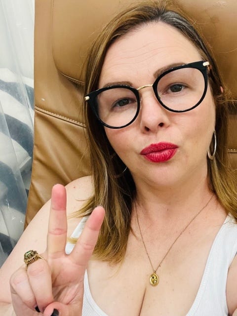 A selfie of Amber. She has her lips pursed toward the camera in a kissy face pose. She wears bright red lipstick. Her hand is making a peace sign gesture.