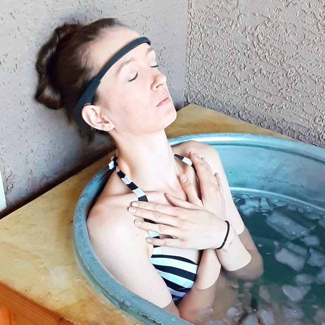 Young woman with arms crossed over her heart meditates in ice bath