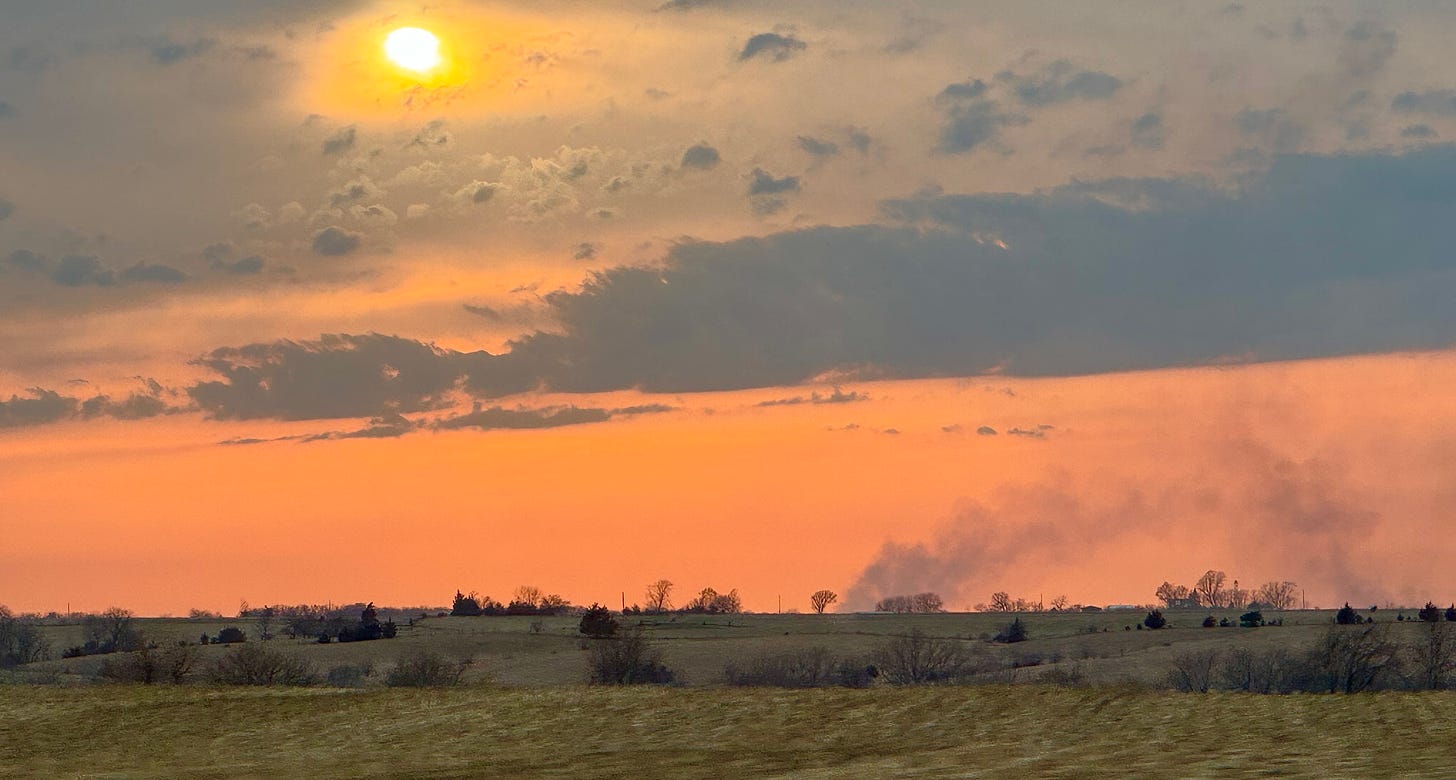 Smoke plumes on the horizon at sunset, in a rural landscape