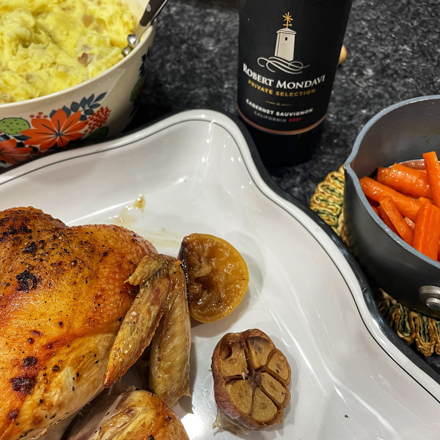 Roast chicken dinner complete with mashed potatoes, boiled carrots, and a bottle of cabernet sauvignon wine.