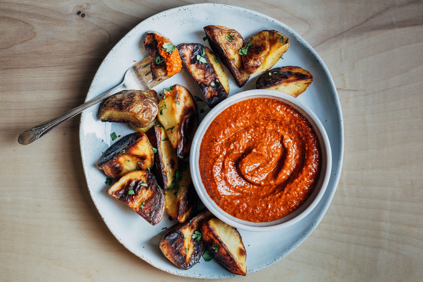 A plate with roasted potatoes with a small bowl of romesco sauce in the center. 