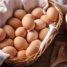 This may contain: a basket filled with brown eggs next to wooden spoons and an egg shell on a table