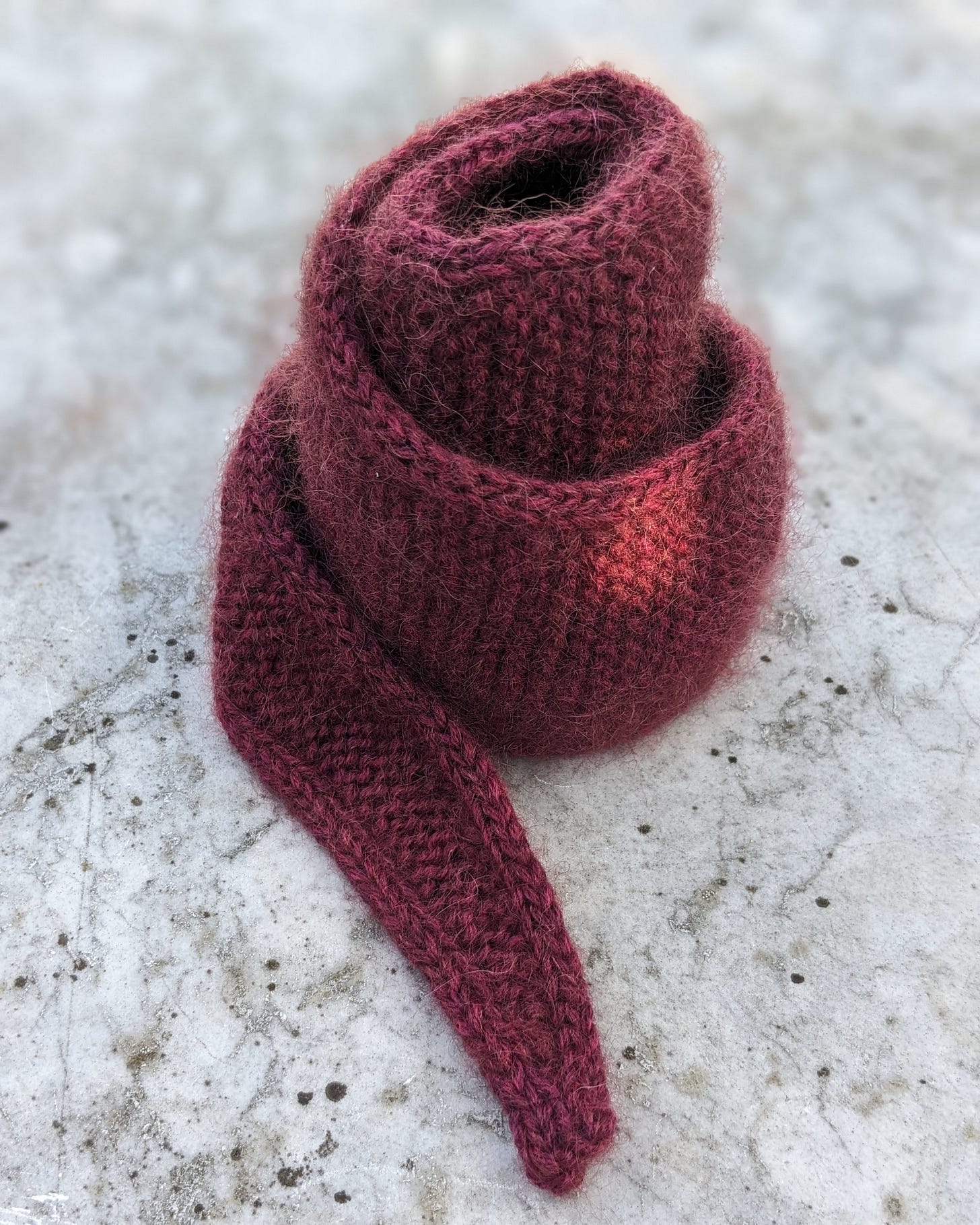 A burgundy red knitted scarf, coiled in a spiral