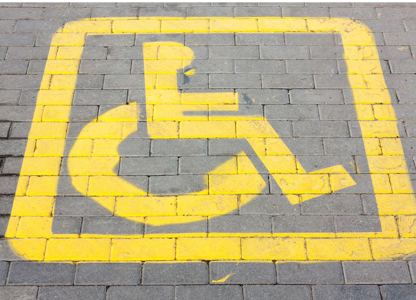 Yellow wheelchair symbol painted on brick pavement