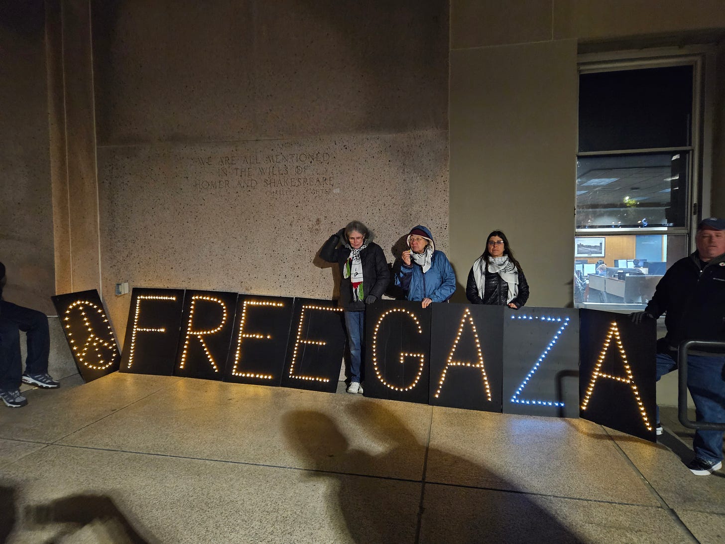 Three people stand behind tall black placards with lights mounted on them that spell out FREE GAZA.