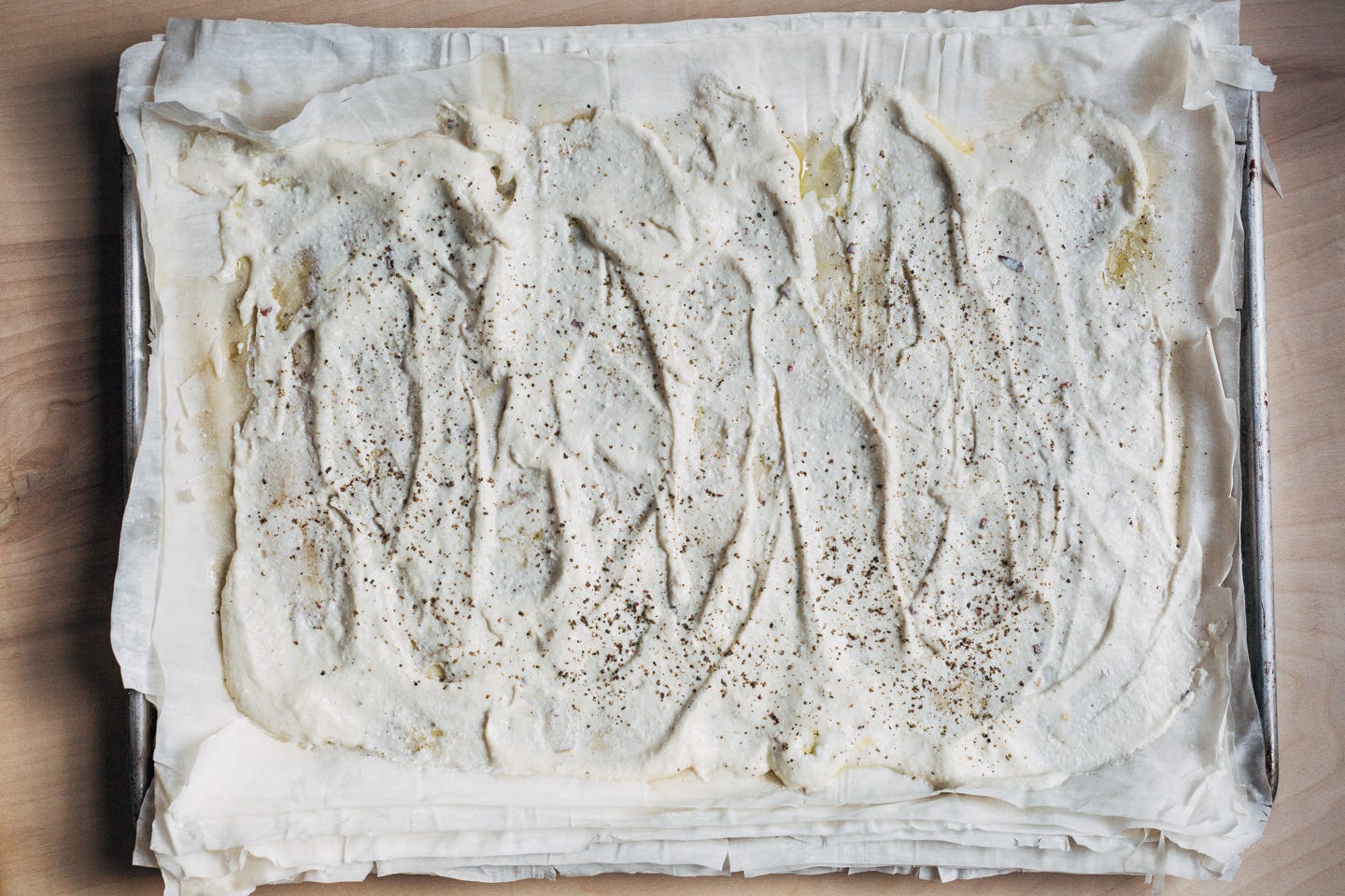 Phyllo dough on a sheet pan with ricotta smeared on top.