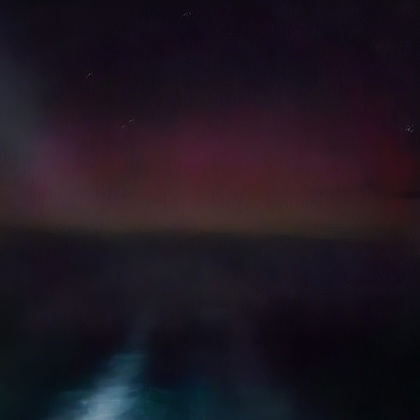 Night sky with pink northern lights above a dark sea