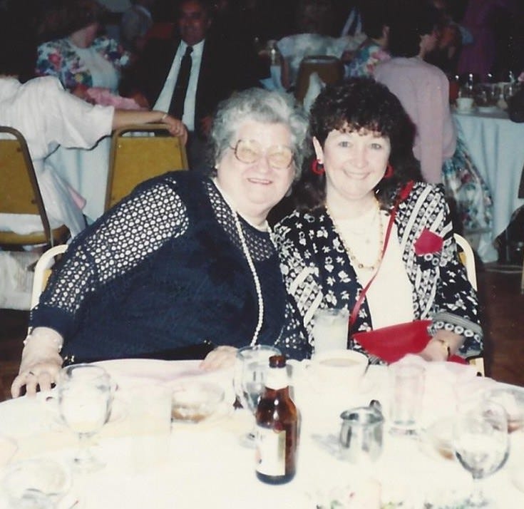 70-ish woman and 40-ish woman seated at a table at a wedding look ready to party