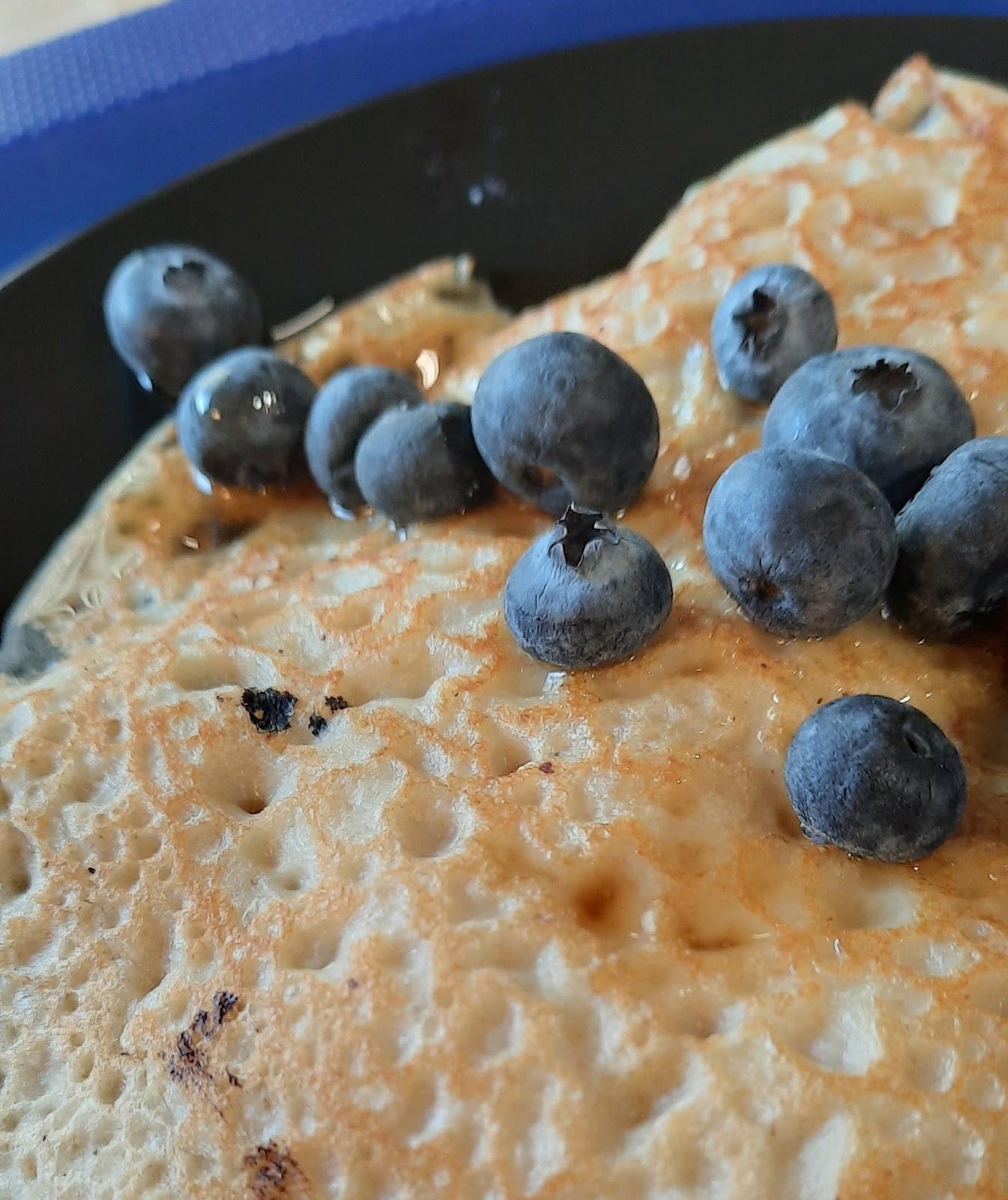 Blueberries with syrup on light brown and pale yellow pancakes on a black plate.