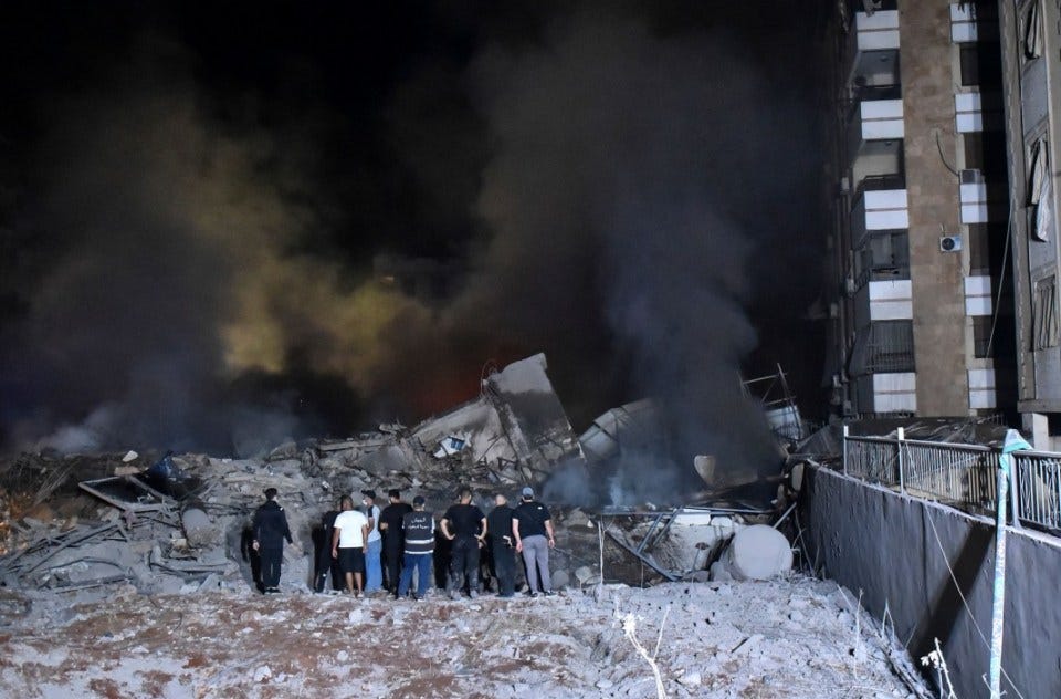 Lebanese civilians and rescue workers look on as plumes of black smoke erupt from a residential block