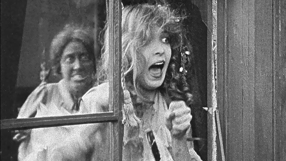 Silent actress Lillian Gish screams at a window in D.W. Griffith's 1915 film The Birth of the Nation. In the background an actor in black-face grimaces